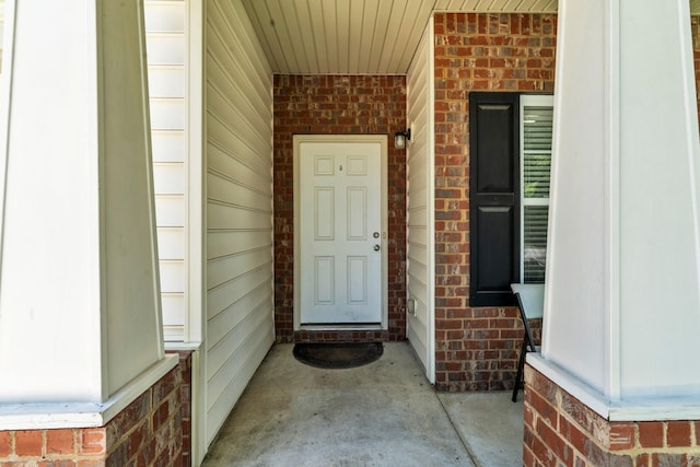 doorway to property featuring covered porch and brick siding