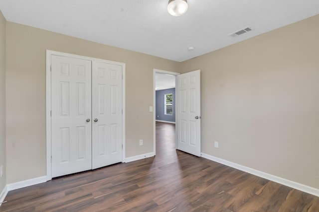 unfurnished bedroom with a closet, dark wood finished floors, visible vents, and baseboards