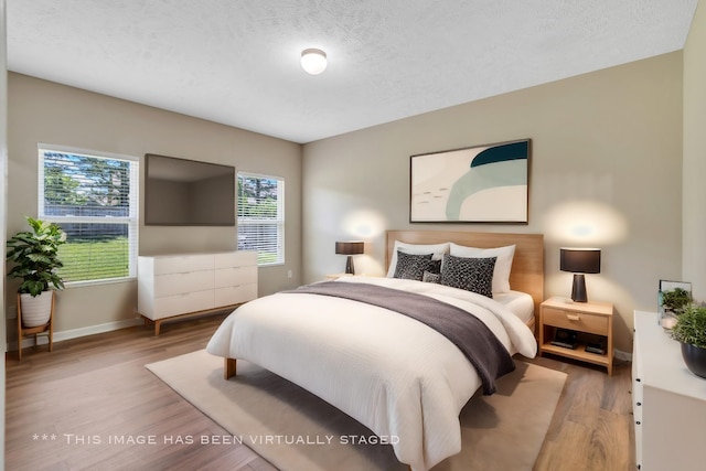 bedroom with a textured ceiling, baseboards, and wood finished floors