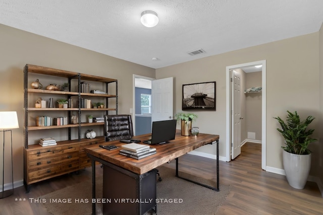 office area with dark wood-style floors, visible vents, a textured ceiling, and baseboards