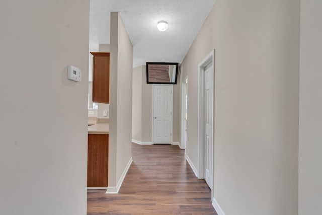 hall with a textured ceiling, baseboards, and wood finished floors