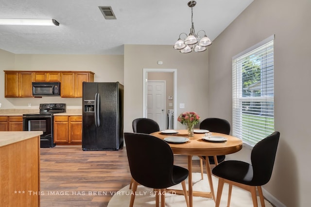 kitchen with light countertops, visible vents, brown cabinetry, wood finished floors, and black appliances