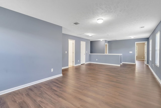 empty room with a textured ceiling, dark wood-style flooring, visible vents, baseboards, and attic access