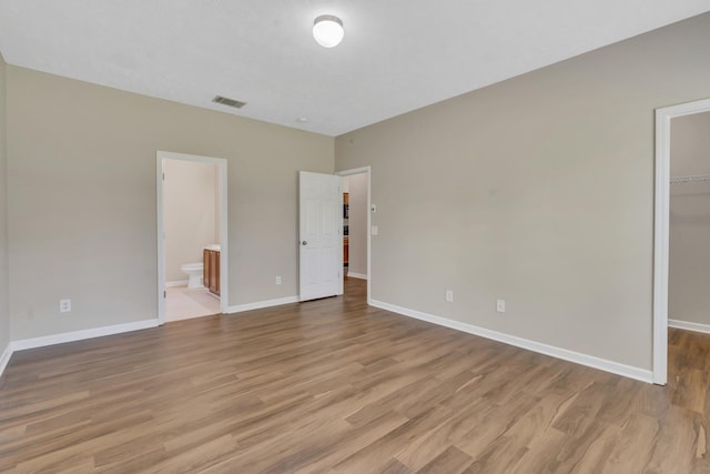 unfurnished bedroom with wood finished floors, visible vents, baseboards, a spacious closet, and a closet