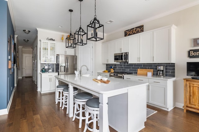 kitchen with appliances with stainless steel finishes, a breakfast bar area, dark wood-style flooring, a kitchen island with sink, and light countertops