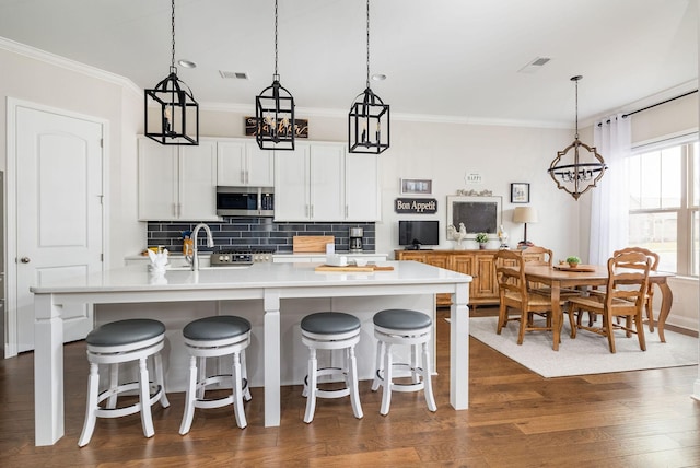 kitchen with dark wood finished floors, light countertops, stainless steel microwave, visible vents, and decorative backsplash