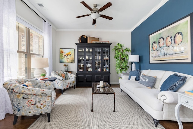 living room featuring wood finished floors, a ceiling fan, baseboards, visible vents, and crown molding