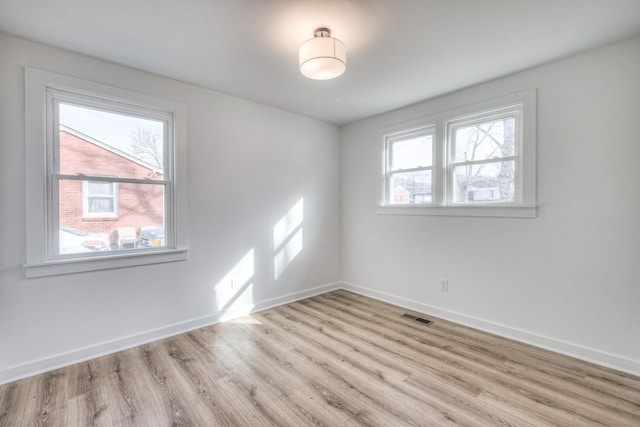 unfurnished room featuring a healthy amount of sunlight, baseboards, visible vents, and wood finished floors