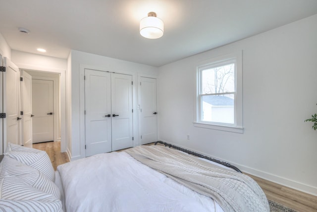 bedroom with light wood-style floors, multiple closets, recessed lighting, and baseboards