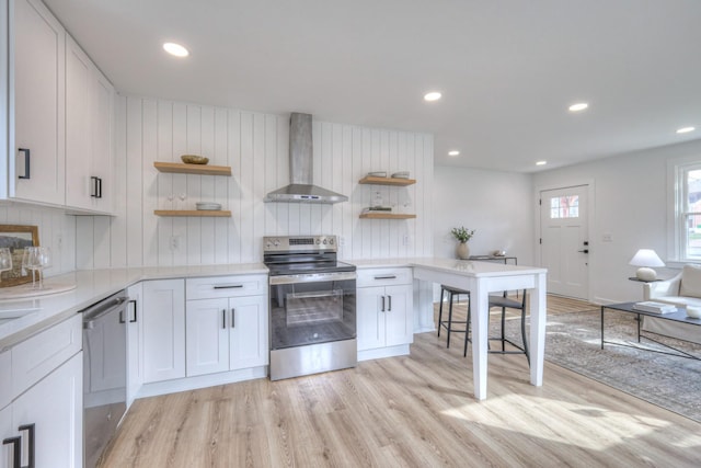 kitchen featuring light wood finished floors, open shelves, light countertops, appliances with stainless steel finishes, and wall chimney range hood