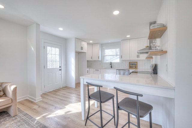 kitchen featuring stainless steel appliances, tasteful backsplash, light wood-style flooring, white cabinetry, and a peninsula