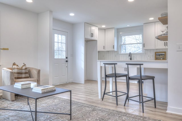 kitchen featuring recessed lighting, decorative backsplash, white cabinetry, a sink, and light wood-type flooring