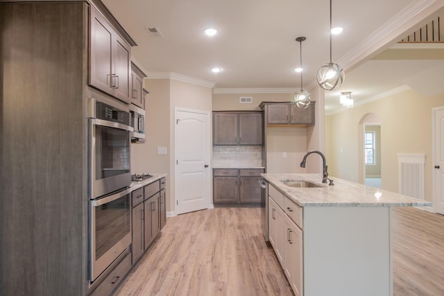 kitchen with a sink, stainless steel appliances, light wood-type flooring, and arched walkways