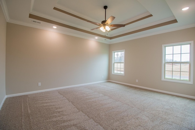 empty room with baseboards, visible vents, crown molding, a raised ceiling, and light colored carpet