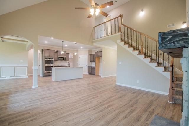 unfurnished living room with visible vents, ceiling fan, light wood-type flooring, stairs, and ornamental molding