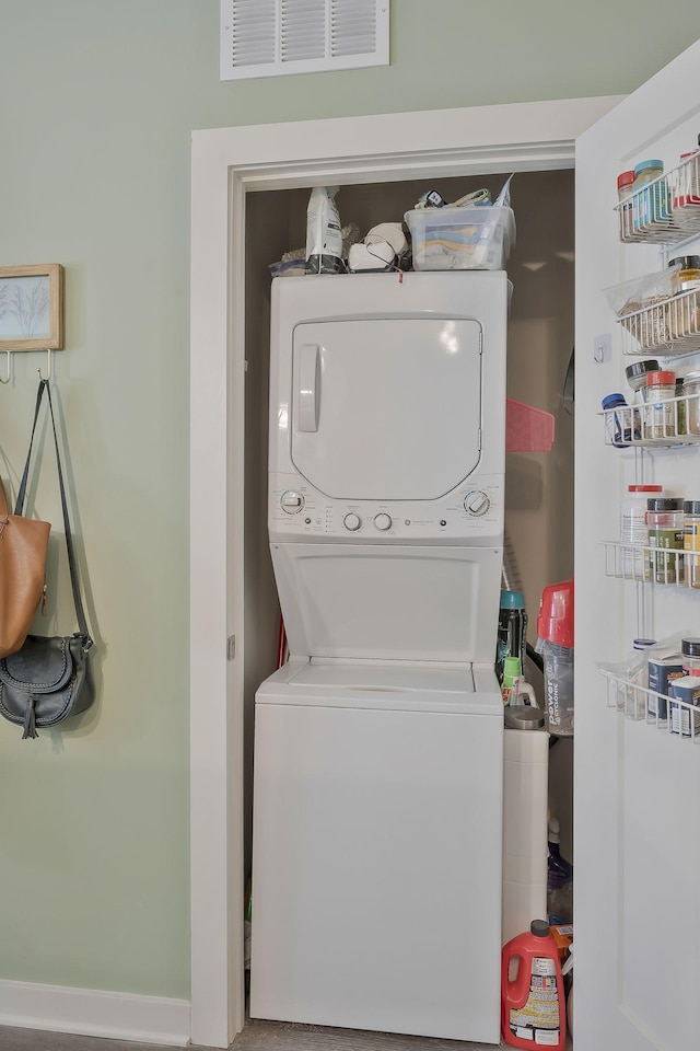 washroom with stacked washing maching and dryer, visible vents, and laundry area