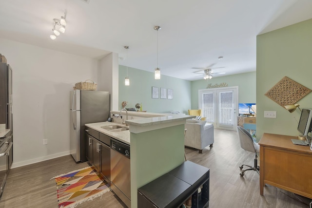 kitchen with stainless steel appliances, light countertops, hanging light fixtures, light wood-style floors, and open floor plan