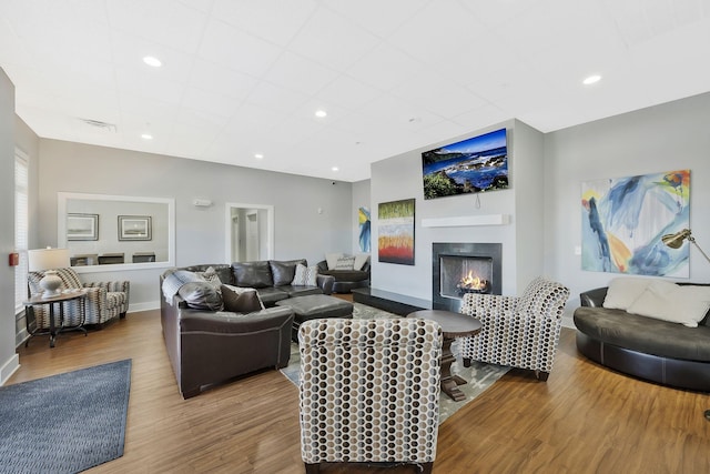 living area featuring recessed lighting, visible vents, wood finished floors, a warm lit fireplace, and baseboards