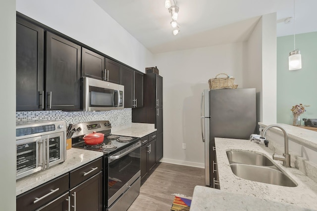 kitchen featuring stainless steel appliances, hanging light fixtures, decorative backsplash, a sink, and light wood-type flooring