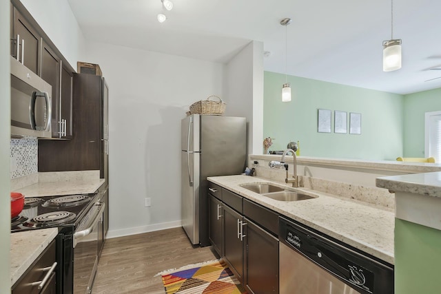 kitchen with appliances with stainless steel finishes, light wood-type flooring, pendant lighting, and a sink