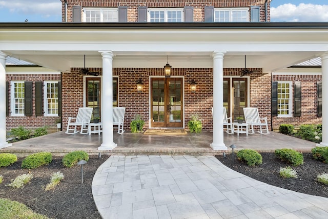 view of exterior entry featuring a porch, french doors, and brick siding