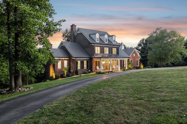 view of front of property featuring driveway, a chimney, a front lawn, and brick siding