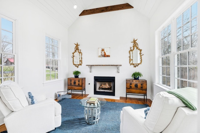 living room with vaulted ceiling with beams, a warm lit fireplace, and wood finished floors