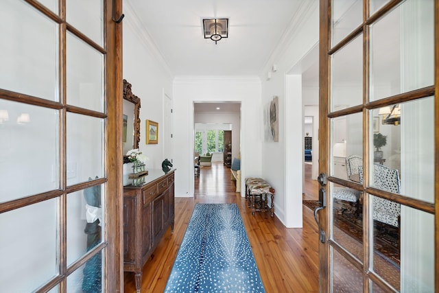 corridor with ornamental molding, french doors, and light wood-style flooring