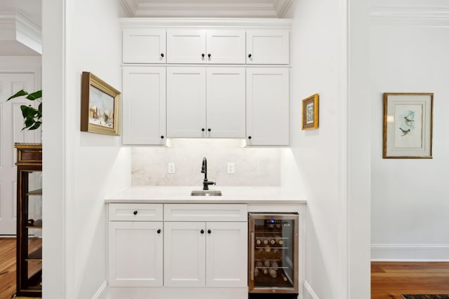 bar featuring wine cooler, wood finished floors, a sink, backsplash, and crown molding