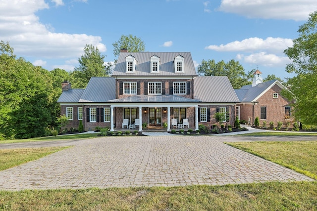 view of front facade with metal roof, a porch, a chimney, and brick siding