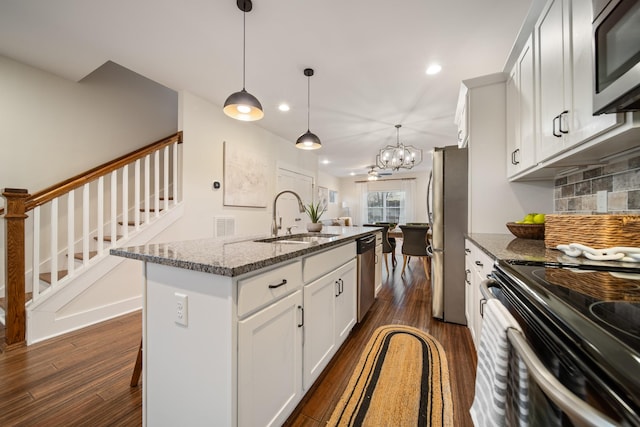 kitchen featuring appliances with stainless steel finishes, dark stone counters, dark wood finished floors, and a sink