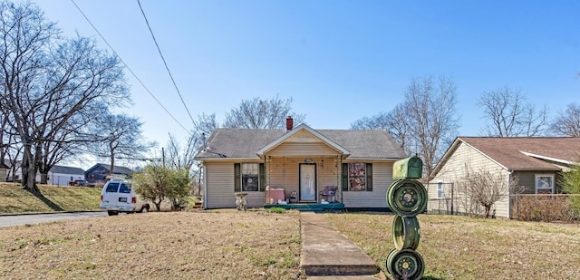 bungalow featuring roof with shingles, a chimney, a front lawn, and fence