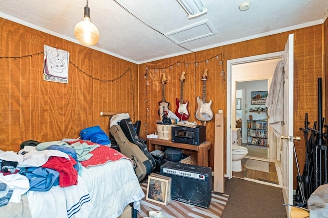 carpeted bedroom with wooden walls, crown molding, attic access, a textured ceiling, and ensuite bath