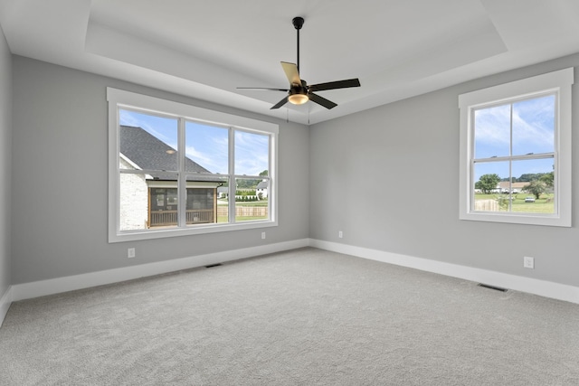 unfurnished room with a tray ceiling, visible vents, and carpet flooring