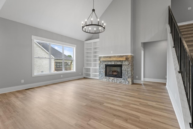 unfurnished living room featuring built in features, light wood-style flooring, an inviting chandelier, a stone fireplace, and stairs