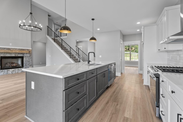 kitchen with a stone fireplace, gray cabinetry, a sink, white cabinets, and appliances with stainless steel finishes