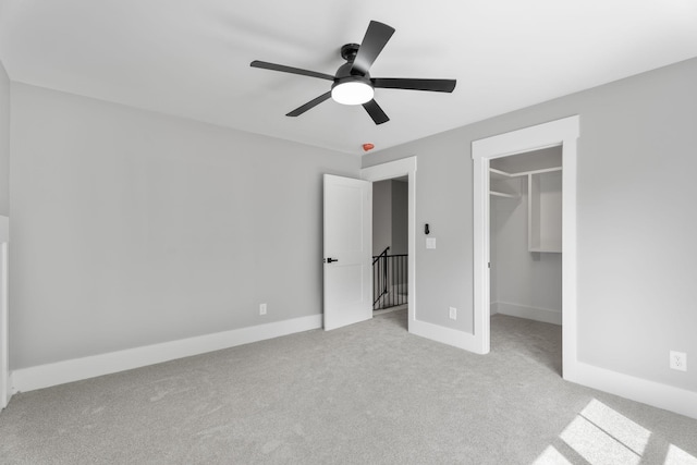 unfurnished bedroom with baseboards, ceiling fan, carpet, a walk in closet, and a closet