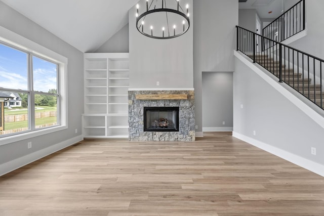 unfurnished living room featuring baseboards, built in shelves, light wood-style flooring, an inviting chandelier, and a fireplace