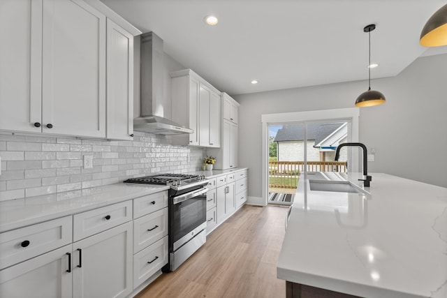 kitchen with wall chimney exhaust hood, a sink, stainless steel range with gas cooktop, white cabinetry, and backsplash