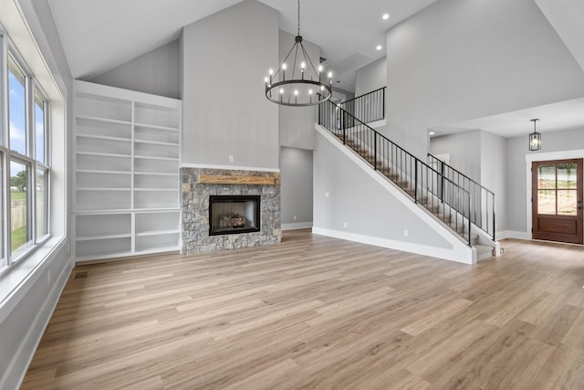 unfurnished living room featuring an inviting chandelier, light wood-style floors, a stone fireplace, baseboards, and stairs