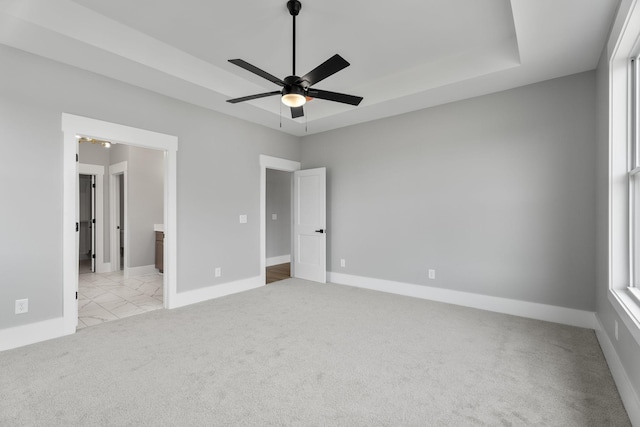 unfurnished bedroom with a raised ceiling, light colored carpet, baseboards, and multiple windows