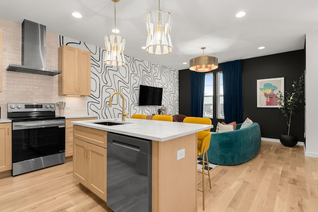 kitchen with a sink, appliances with stainless steel finishes, wall chimney range hood, and light wood-style flooring