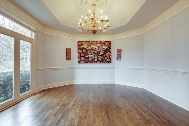 spare room with a notable chandelier, baseboards, a raised ceiling, and wood finished floors