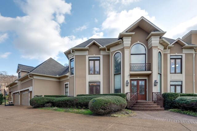 view of front facade with a garage, driveway, a shingled roof, french doors, and stucco siding