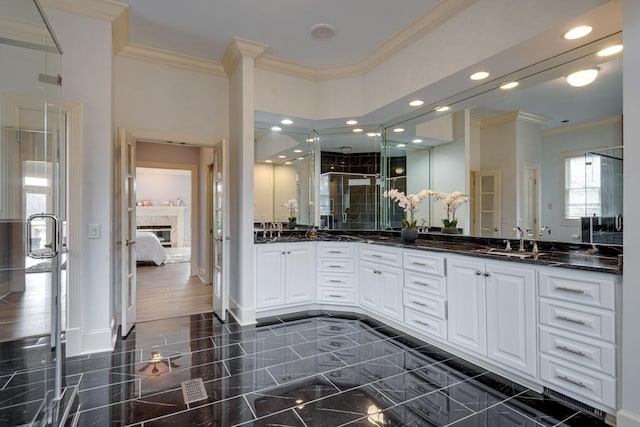 ensuite bathroom with double vanity, a glass covered fireplace, a sink, a shower stall, and baseboards