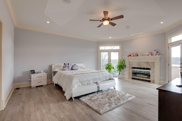 bedroom with baseboards, crown molding, light wood finished floors, and a premium fireplace