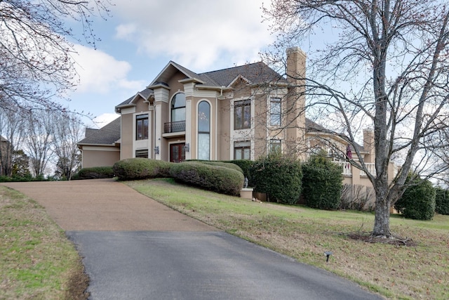 view of front facade with driveway, a chimney, a front lawn, and stucco siding