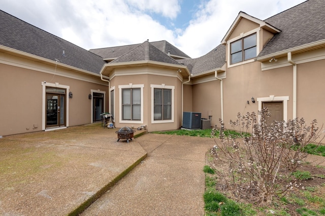 rear view of house featuring a patio area, a shingled roof, a fire pit, and stucco siding