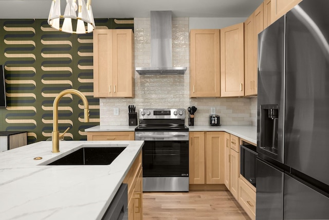 kitchen featuring stainless steel appliances, light wood-type flooring, wall chimney range hood, light brown cabinets, and a sink