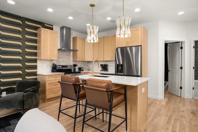 kitchen with light wood finished floors, wall chimney exhaust hood, appliances with stainless steel finishes, light brown cabinets, and a sink